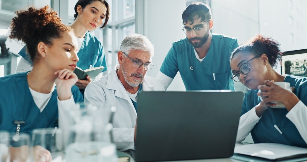 a group of nurses and doctors looking at a computer in a doctor's office