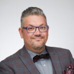 a man with brown-gray hair and glasses wearing a coat and a bow tie