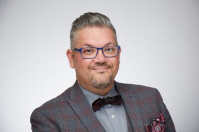 a man with brown-gray hair and glasses wearing a coat and a bow tie